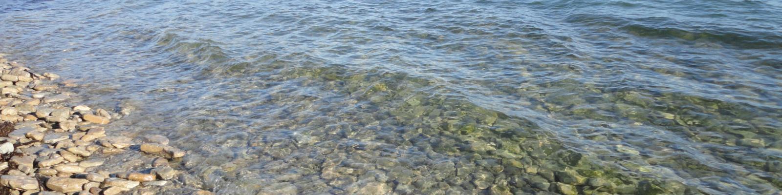 Rocky shoreline meeting a clear, calm blue lake under a clear sky.
