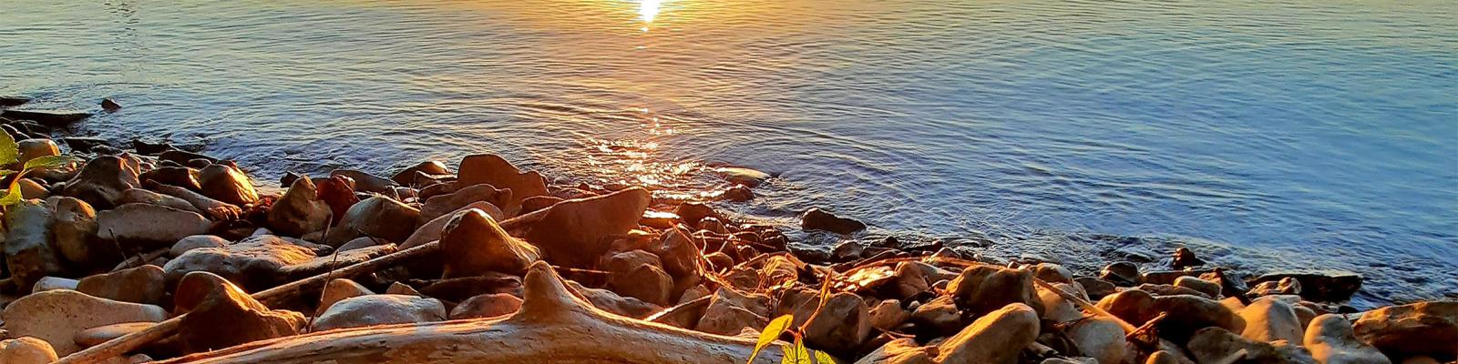 Rocky shoreline at sunset with warm light reflecting on water.