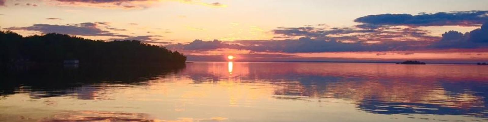 Sunset over a calm lake with vibrant pink and orange clouds.