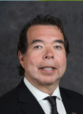 Headshot of a man smiling, wearing a white shirt and a black tie with a black suit jacket.