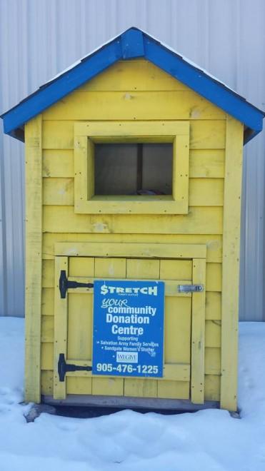 Yellow wooden donation shed with blue roof, standing in snow.