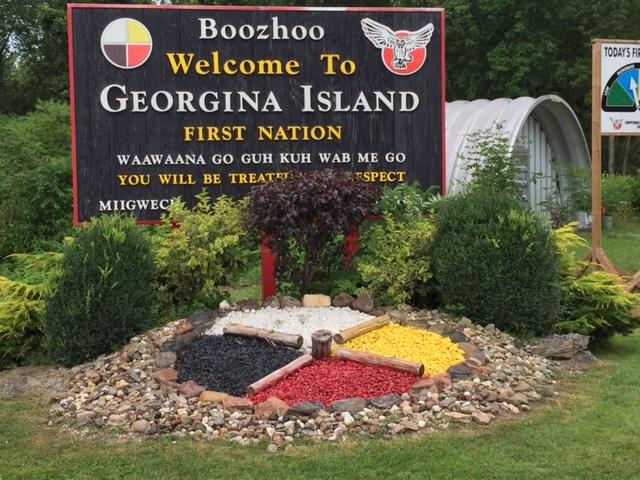 Welcome sign to Georgina Island, with a round symbol divided into quadrants of white, yellow, black and red.