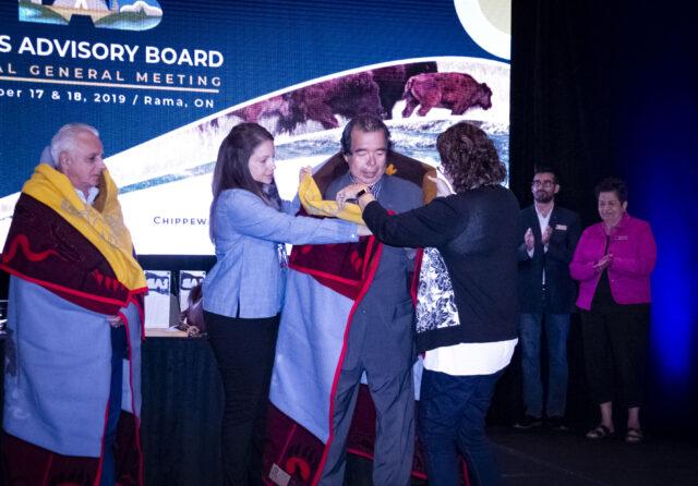 Two people drape blankets over three smiling individuals on stage.